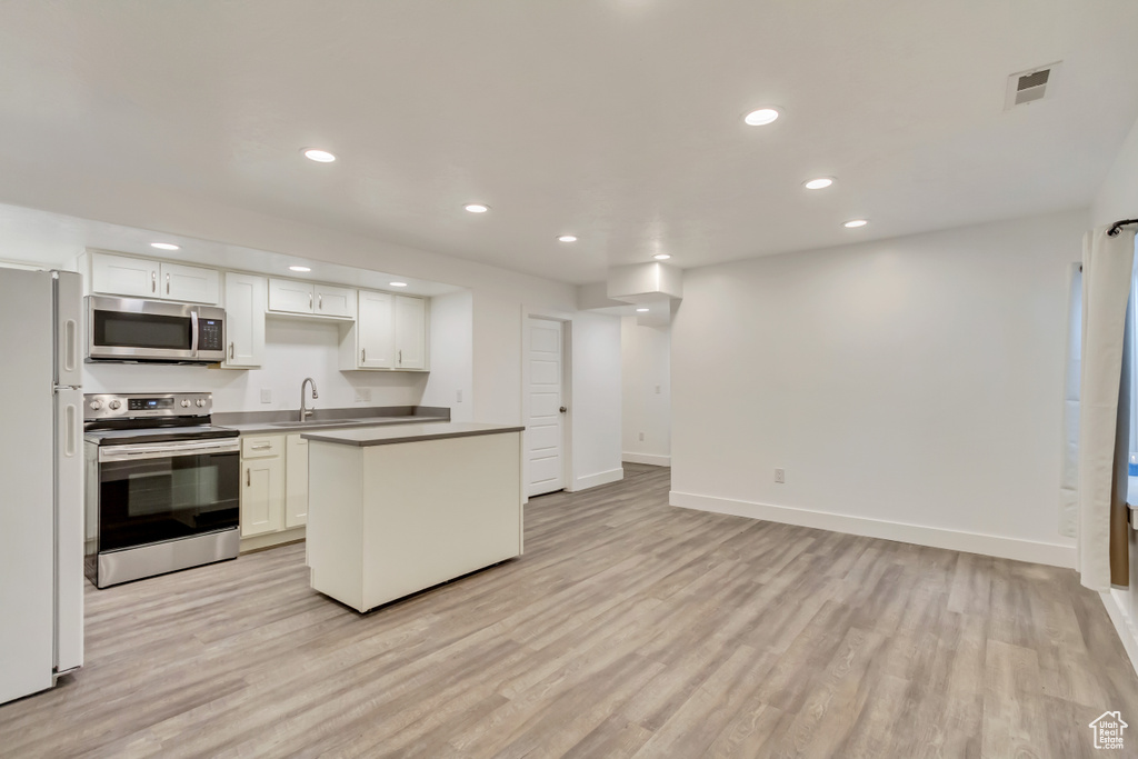 Kitchen featuring appliances with stainless steel finishes, light wood finished floors, a sink, white cabinets, and recessed lighting