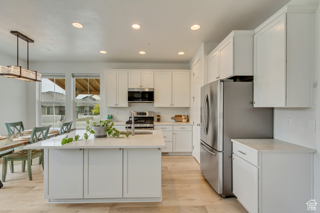 Kitchen featuring appliances with stainless steel finishes, light countertops, white cabinets, decorative backsplash, and light wood finished floors