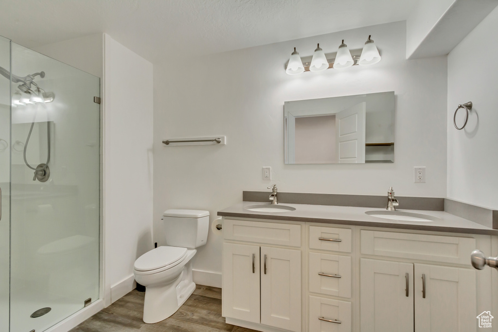 Full bath featuring a shower stall, wood finished floors, toilet, and double vanity