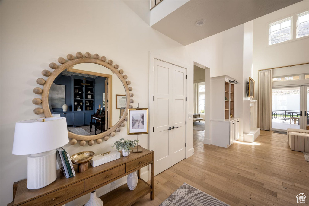 Hall with a towering ceiling, light wood-type flooring, and plenty of natural light