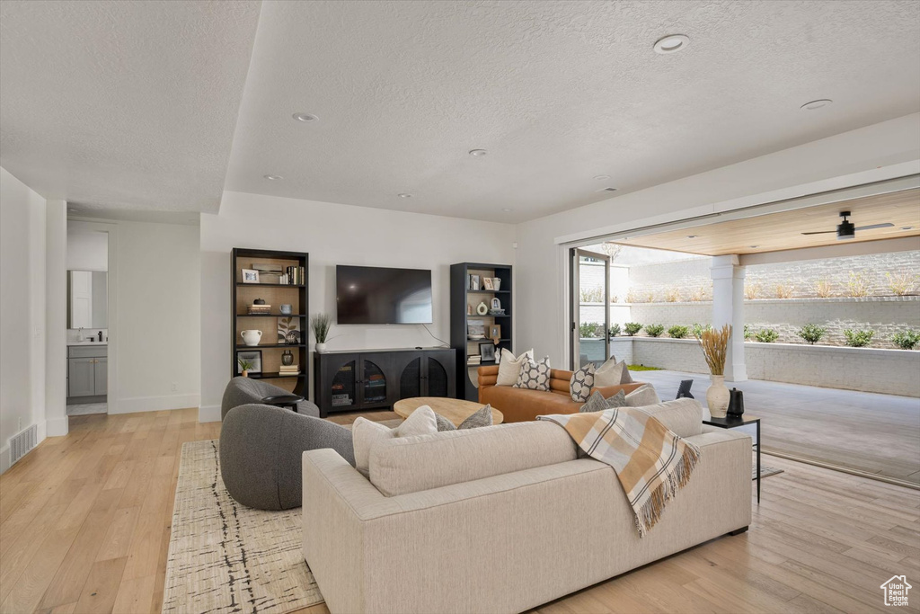 Living area with a textured ceiling, light wood-style flooring, and baseboards