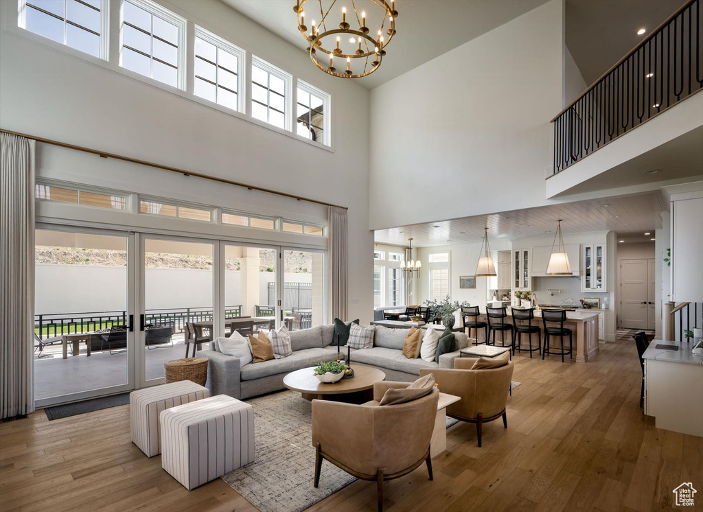 Living room with a chandelier, a high ceiling, light wood-style floors, and healthy amount of natural light