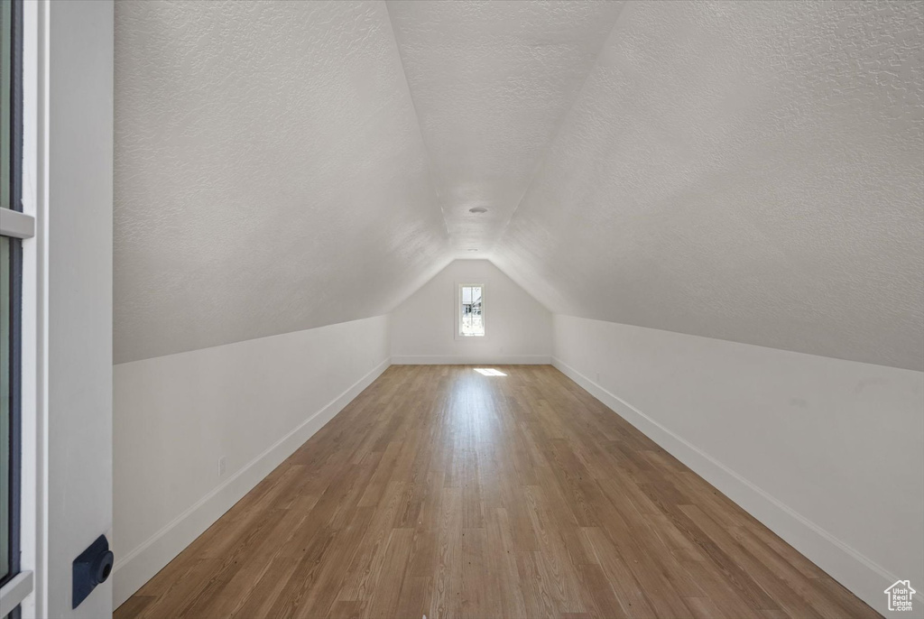 Bonus room with a textured ceiling, vaulted ceiling, wood finished floors, and baseboards