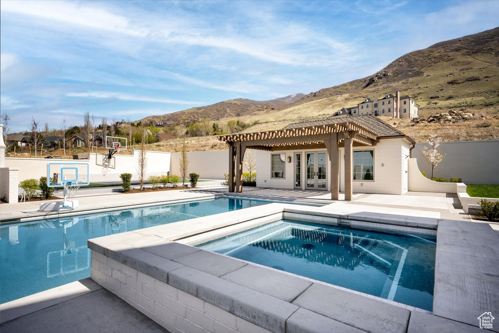 Swimming pool with a mountain view, an in-ground hot tub, french doors, and fence