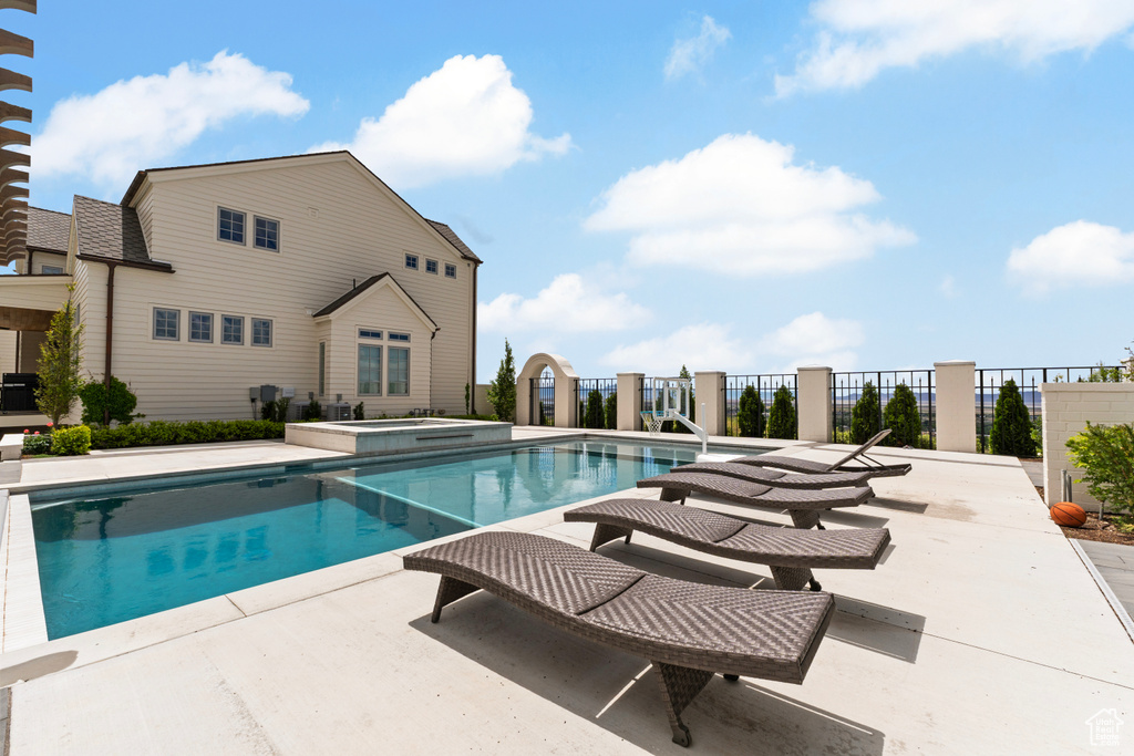 View of swimming pool with a patio area, fence, and a pool with connected hot tub
