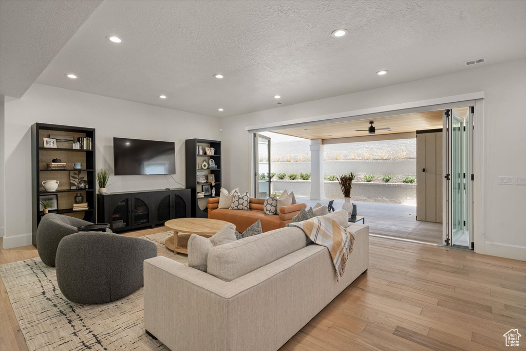 Living room with light wood-type flooring, a textured ceiling, recessed lighting, baseboards, and ceiling fan
