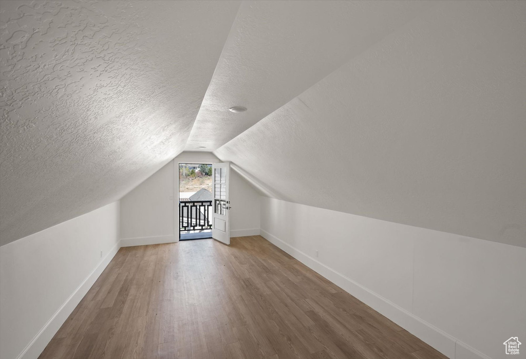 Additional living space with baseboards, a textured ceiling, wood finished floors, and vaulted ceiling