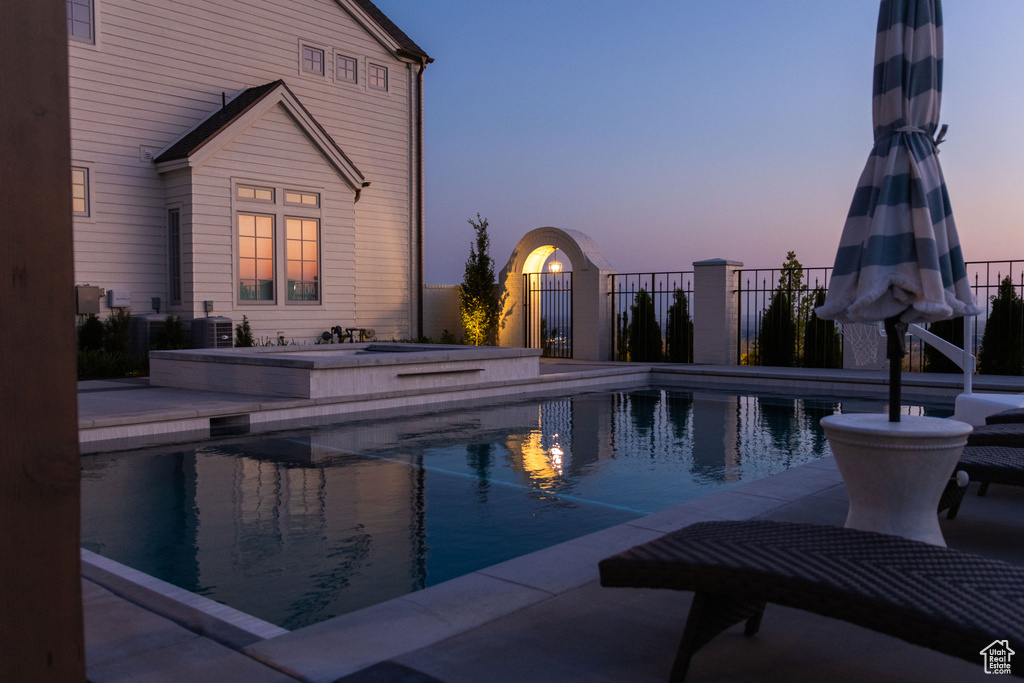 Pool at dusk with a hot tub and fence