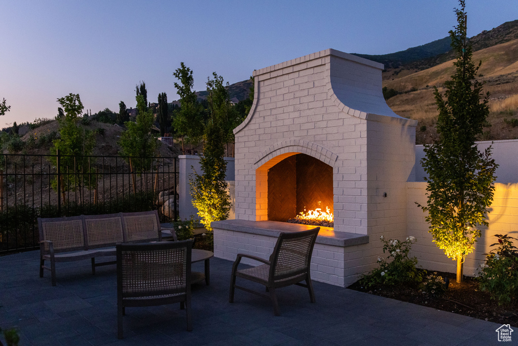 Patio terrace at dusk featuring an outdoor living space with a fireplace, fence, and a mountain view