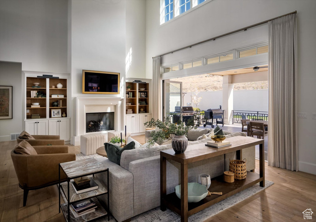 Living area with a high ceiling, a fireplace with raised hearth, wood finished floors, and built in shelves