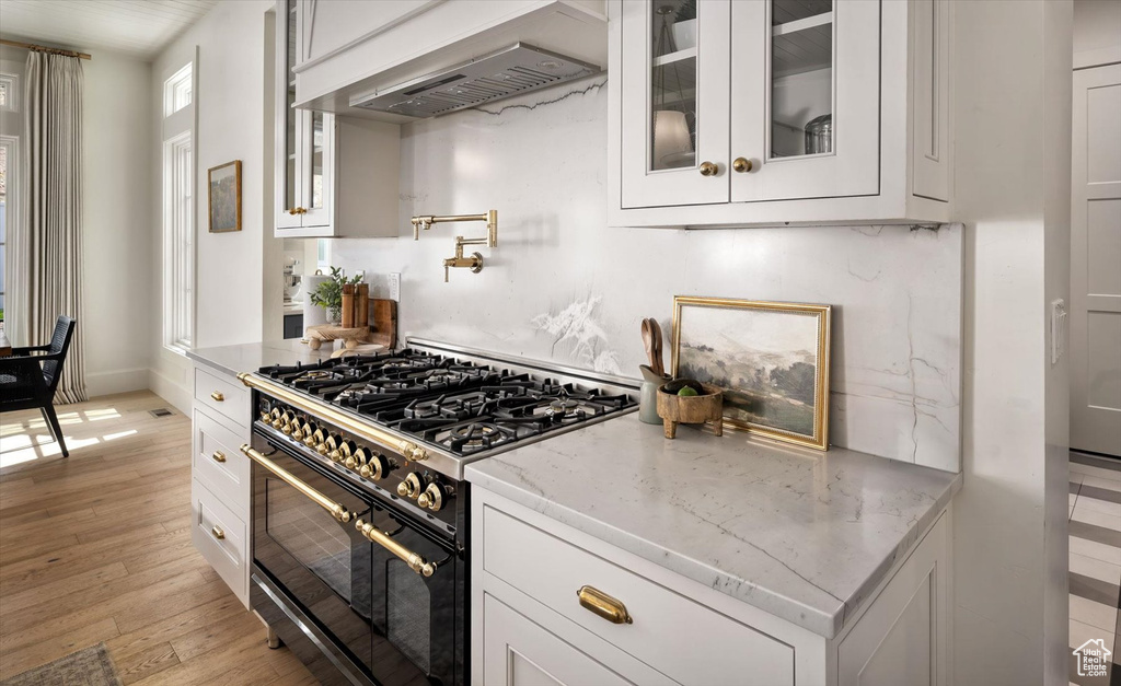 Kitchen with range with two ovens, white cabinetry, light wood-style floors, and glass insert cabinets