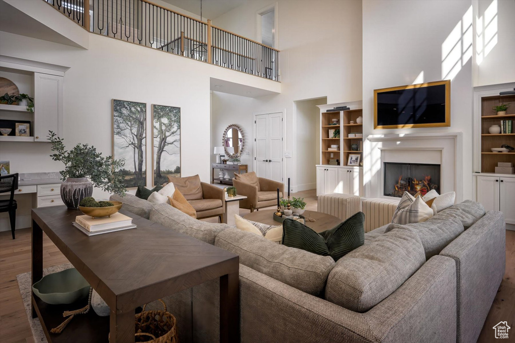 Living room with a towering ceiling, wood finished floors, a warm lit fireplace, baseboards, and built in shelves