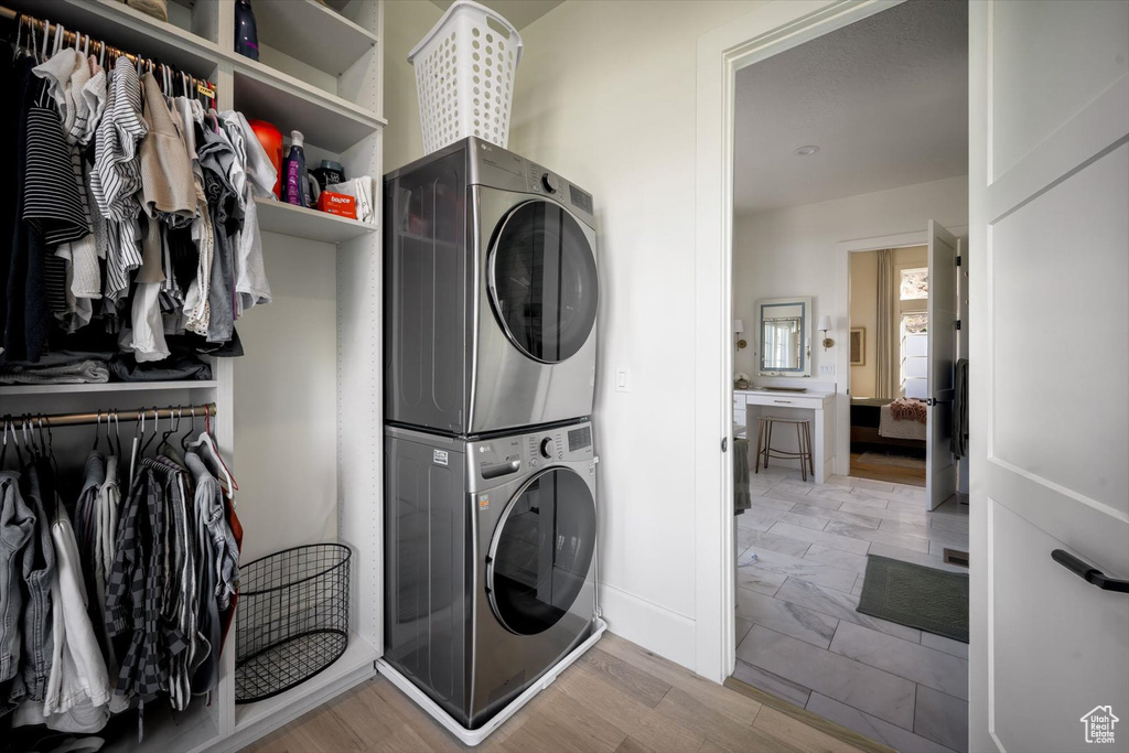 Washroom with stacked washer / drying machine, light wood-style floors, and baseboards