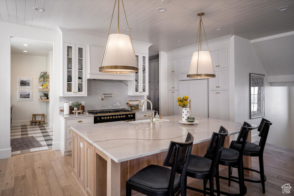 Kitchen featuring a sink, premium range hood, gas range, light wood-style flooring, and white cabinets