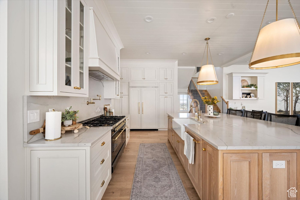 Kitchen featuring stainless steel range, a sink, premium range hood, light wood-style flooring, and glass insert cabinets