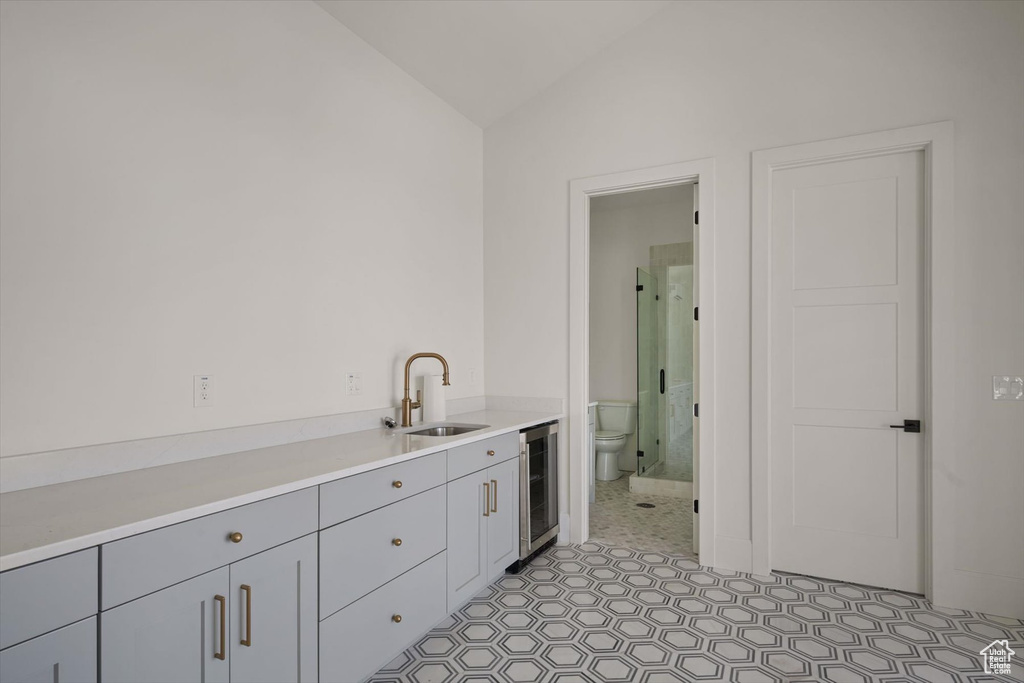 Kitchen featuring beverage cooler, a sink, vaulted ceiling, gray cabinetry, and light countertops