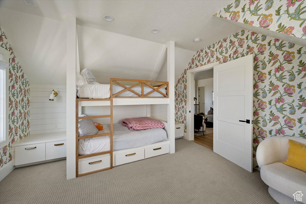 Bedroom featuring wallpapered walls, vaulted ceiling, and light colored carpet