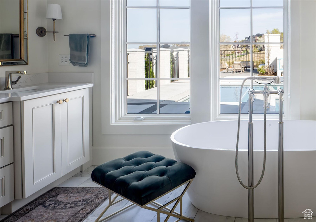 Bathroom with plenty of natural light, vanity, a soaking tub, and marble finish flooring