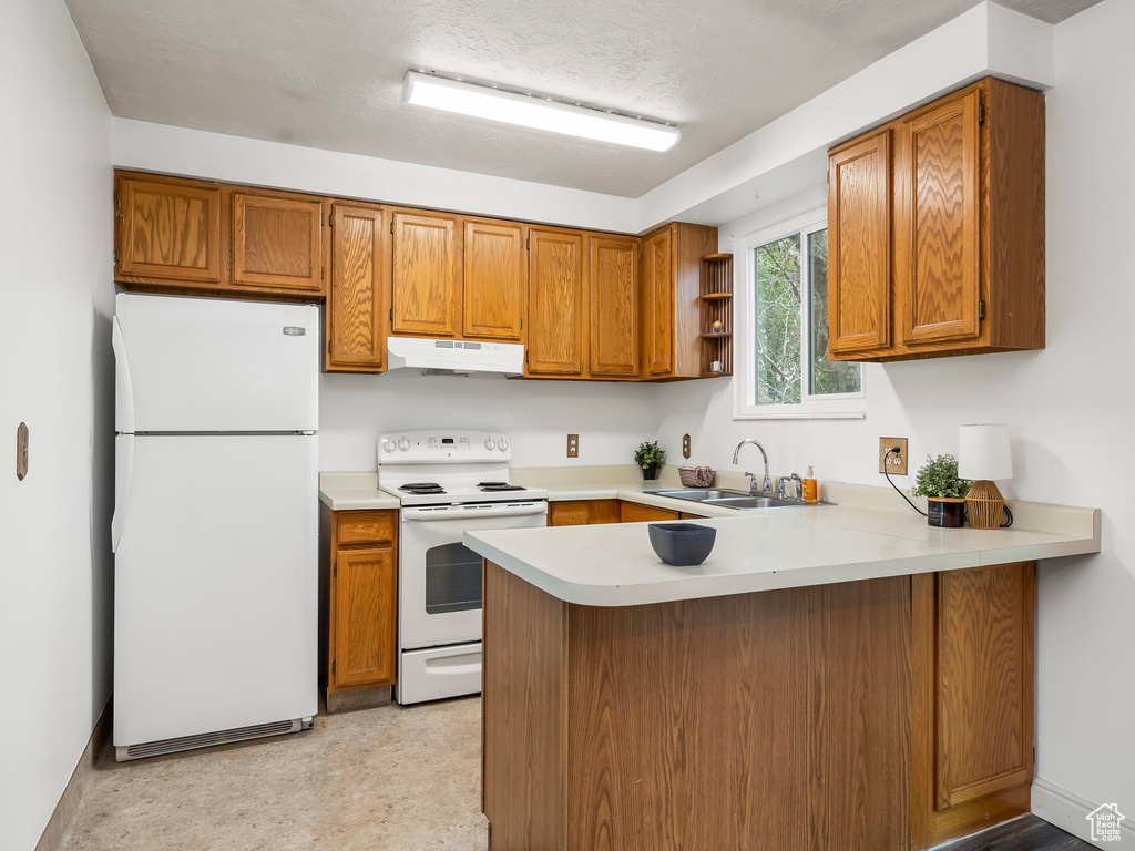 Kitchen with white appliances, a sink, under cabinet range hood, a peninsula, and brown cabinets
