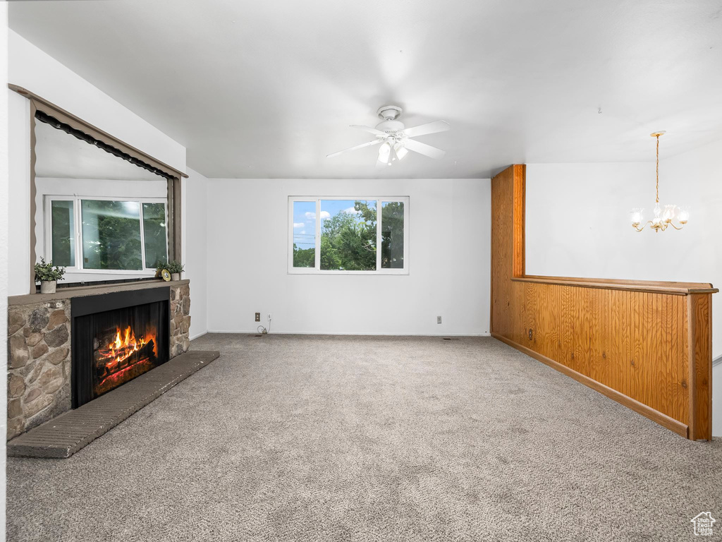 Unfurnished living room featuring a stone fireplace, carpet floors, a chandelier, and ceiling fan