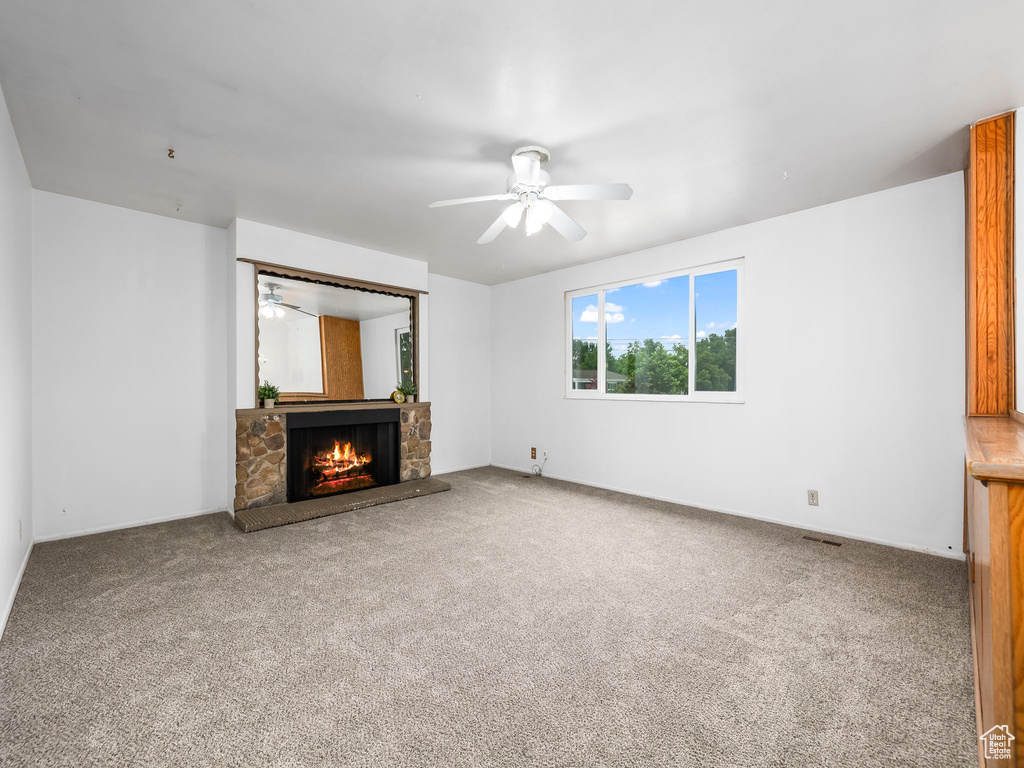 Unfurnished living room with ceiling fan, a fireplace, carpet, and baseboards