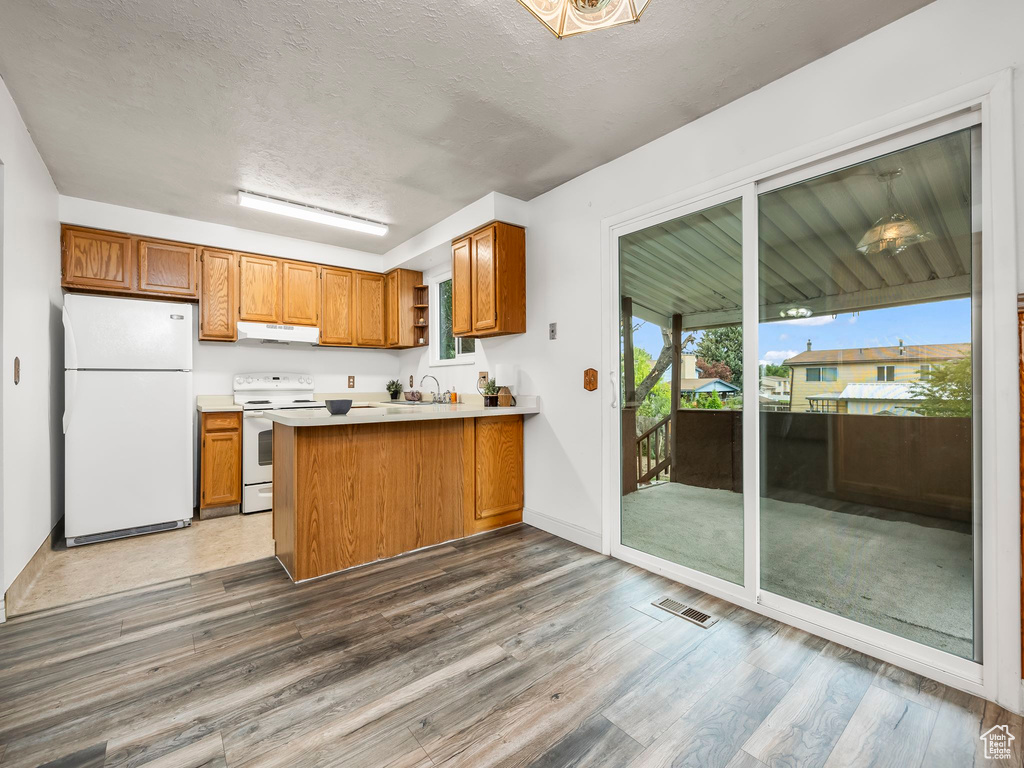 Kitchen with white appliances, under cabinet range hood, wood finished floors, brown cabinets, and a textured ceiling