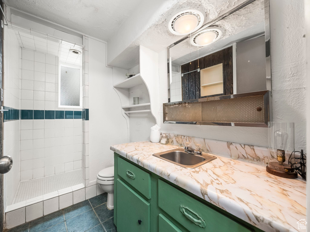 Bathroom with tiled shower, toilet, tile patterned floors, and vanity