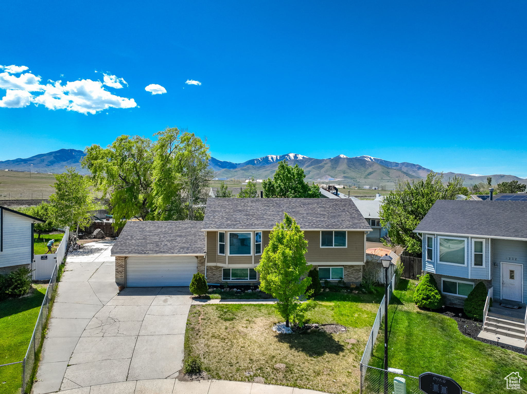 View of front facade featuring a mountain view, concrete driveway, an attached garage, stone siding, and a residential view