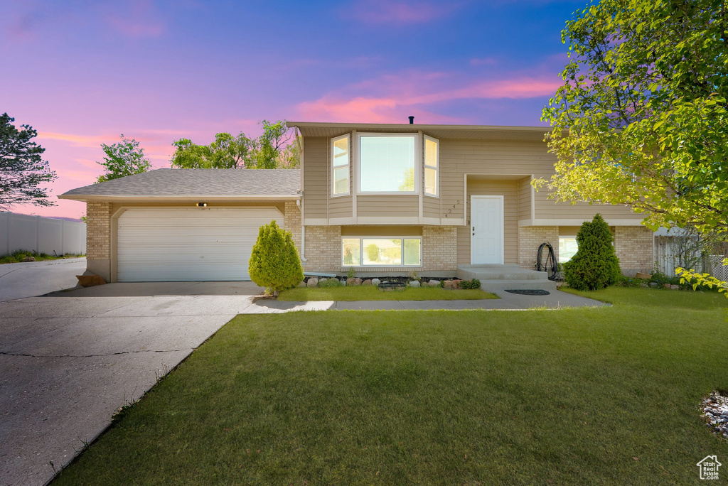Bi-level home with brick siding, driveway, a garage, and a yard