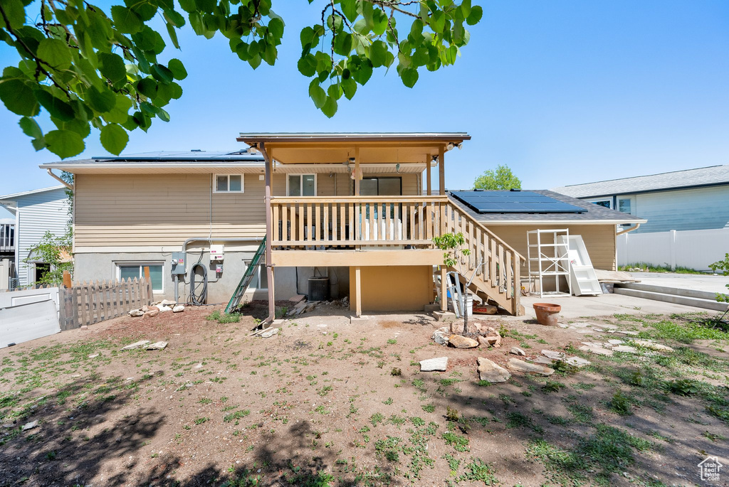 Back of property featuring roof mounted solar panels, stairs, fence, a wooden deck, and central AC unit