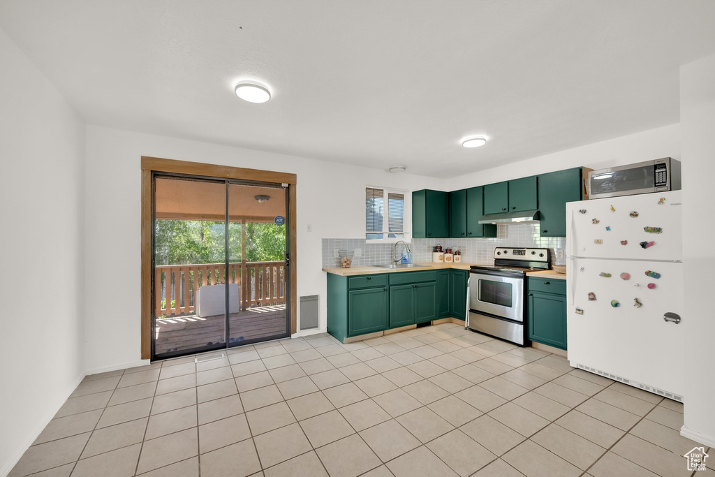 Kitchen with green cabinetry, stainless steel appliances, a sink, under cabinet range hood, and light countertops
