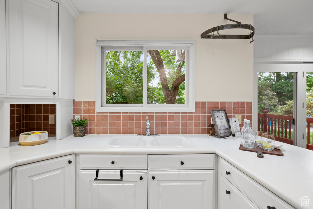 Kitchen with healthy amount of natural light, white cabinetry, a sink, and decorative backsplash