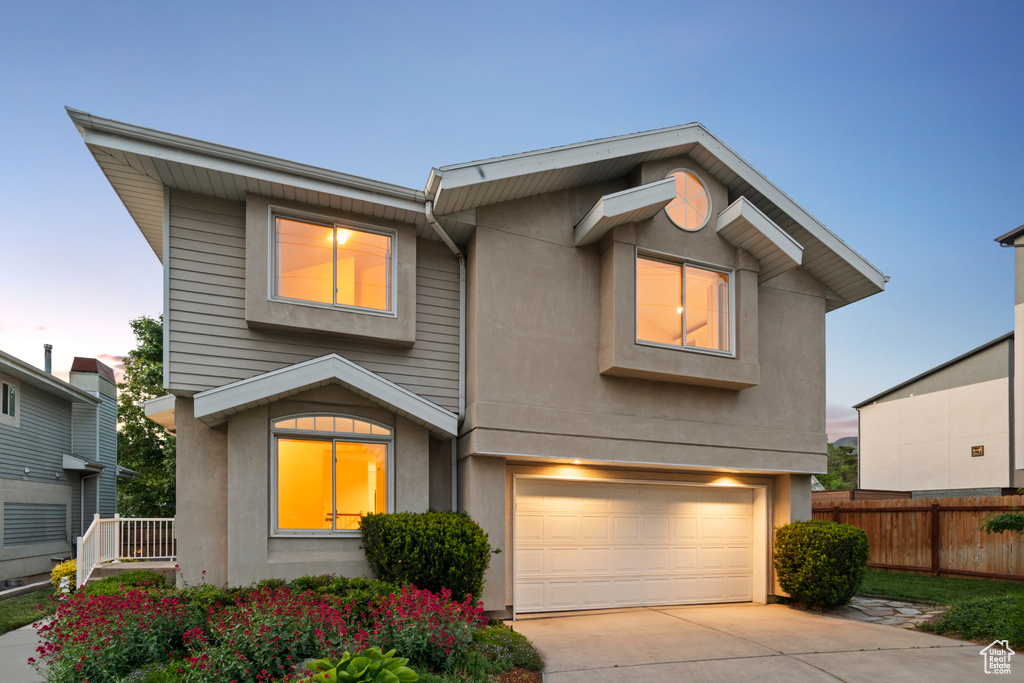 View of front facade with a garage, fence, concrete driveway, and stucco siding