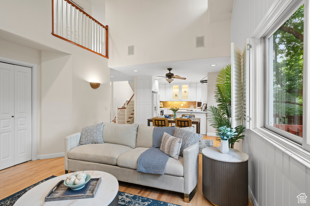 Living room with stairway, a ceiling fan, light wood-style floors, and a high ceiling