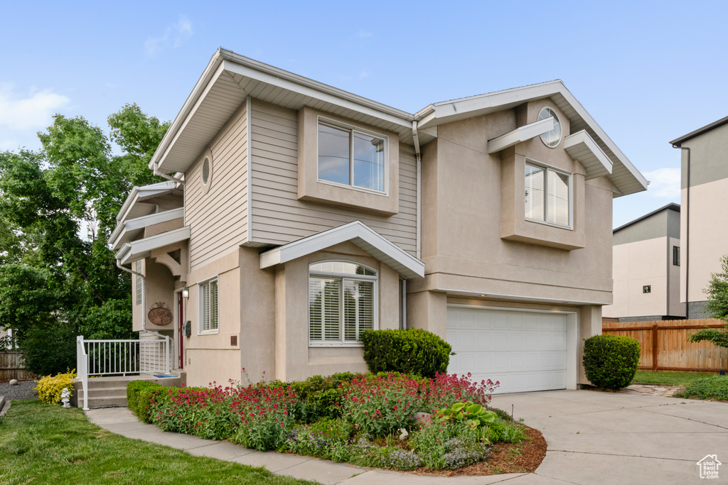 View of property featuring fence, a garage, concrete driveway, and stucco siding