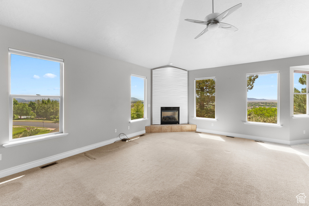 Unfurnished living room with lofted ceiling, a tiled fireplace, baseboards, and carpet flooring