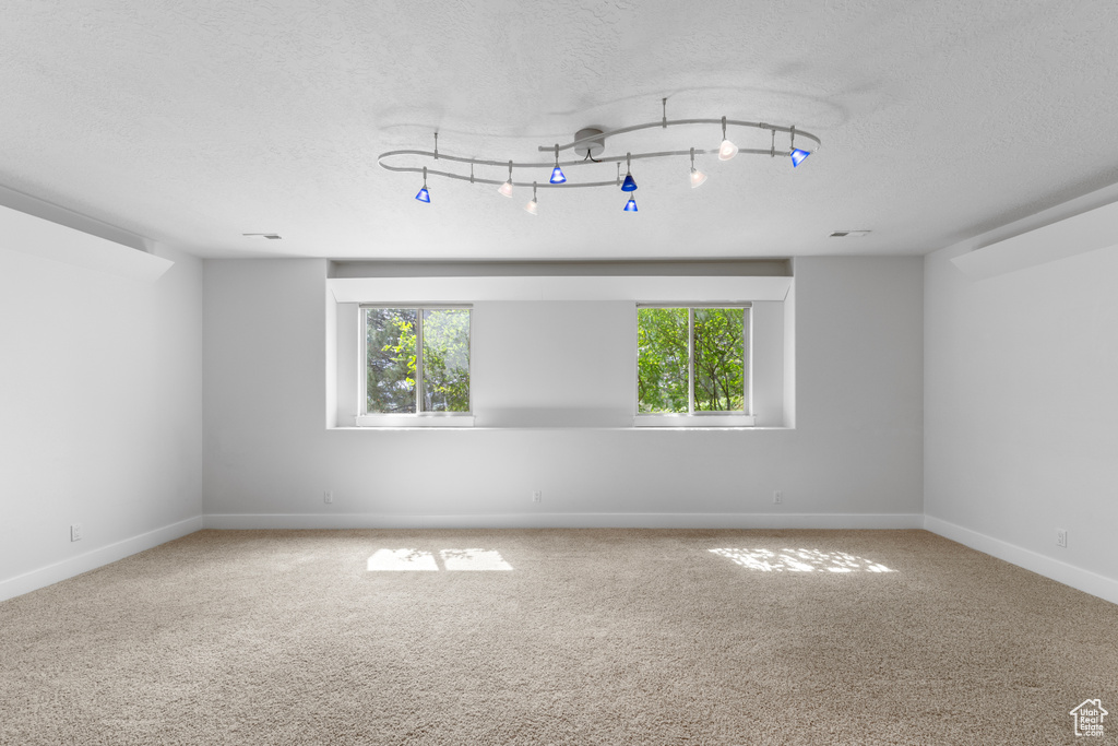 Empty room featuring a textured ceiling, baseboards, and carpet flooring