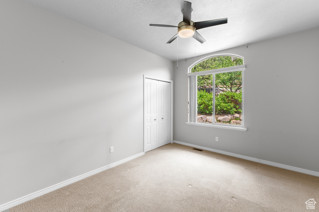 Carpeted spare room with a ceiling fan, baseboards, and a textured ceiling