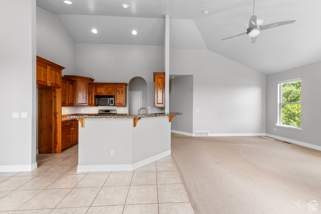 Kitchen with appliances with stainless steel finishes, a breakfast bar, stone counters, high vaulted ceiling, and a ceiling fan