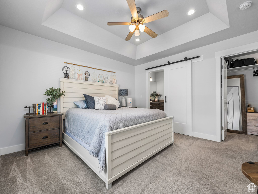 Carpeted bedroom featuring a tray ceiling, a barn door, baseboards, recessed lighting, and ceiling fan