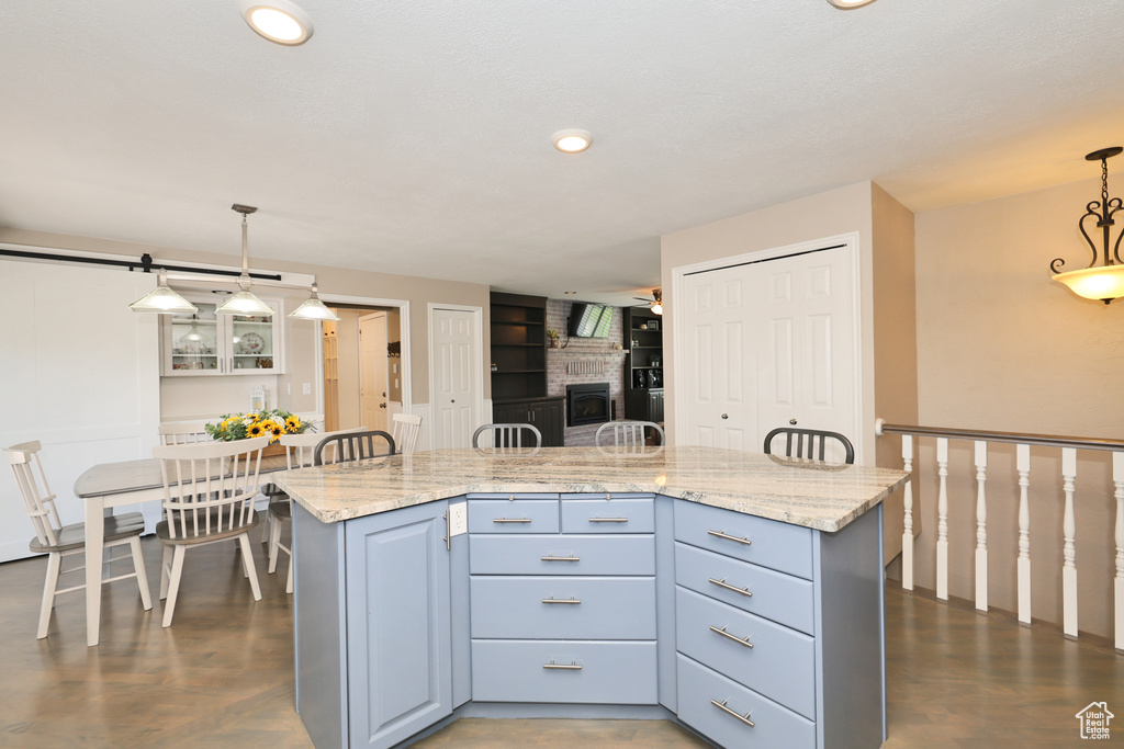 Kitchen with decorative light fixtures, a brick fireplace, light stone counters, recessed lighting, and a center island