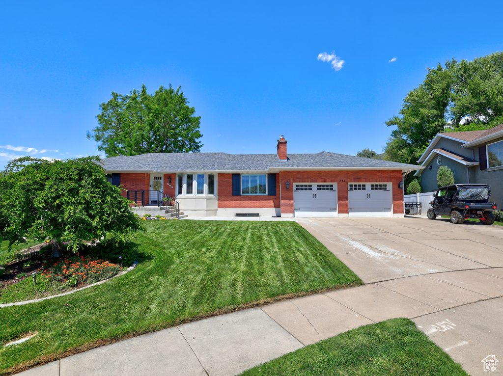 Single story home featuring brick siding, an attached garage, driveway, a chimney, and a front lawn