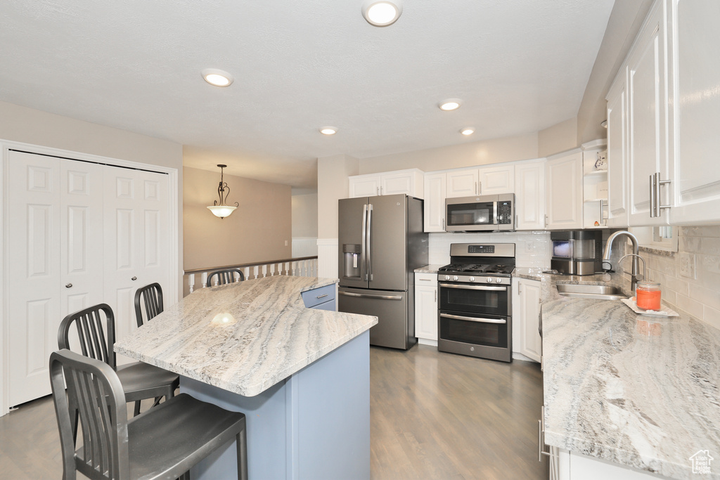 Kitchen featuring appliances with stainless steel finishes, a sink, a kitchen breakfast bar, white cabinetry, and backsplash