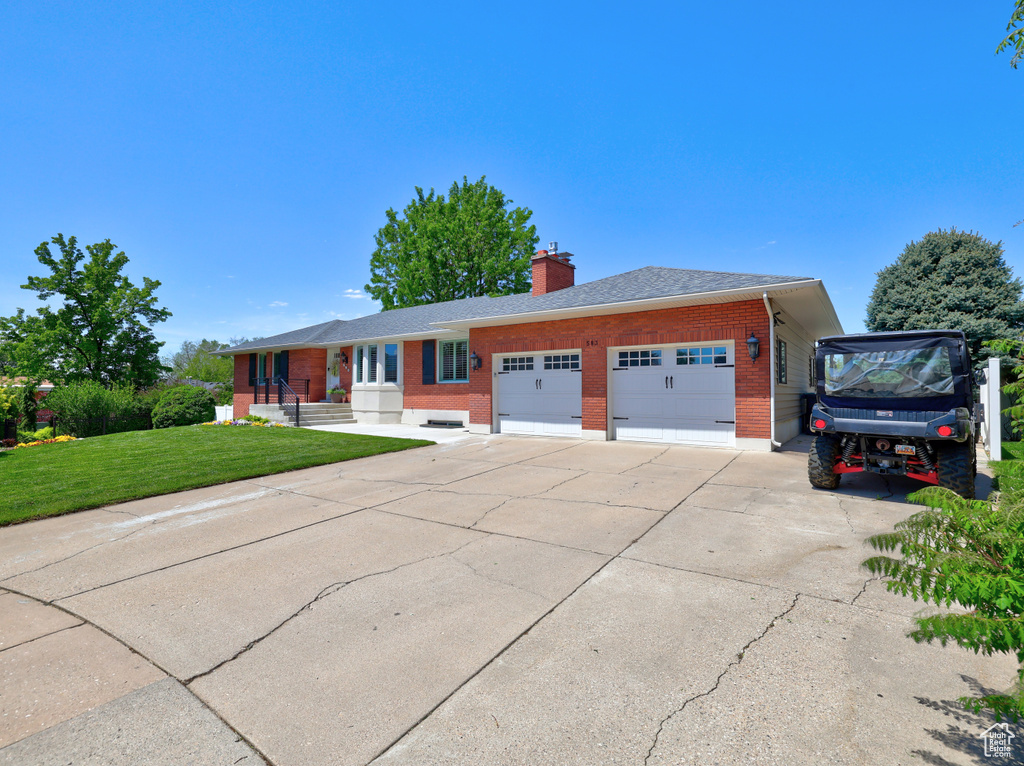 Ranch-style home featuring brick siding, a garage, a front yard, a chimney, and concrete driveway