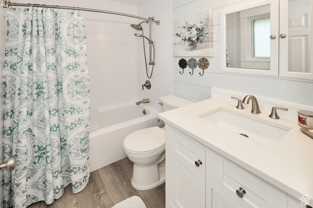 Bathroom with wood finished floors, toilet, shower / bathtub combination with curtain, and vanity