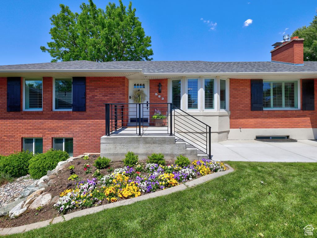 View of front facade featuring a front yard, brick siding, a shingled roof, and a chimney