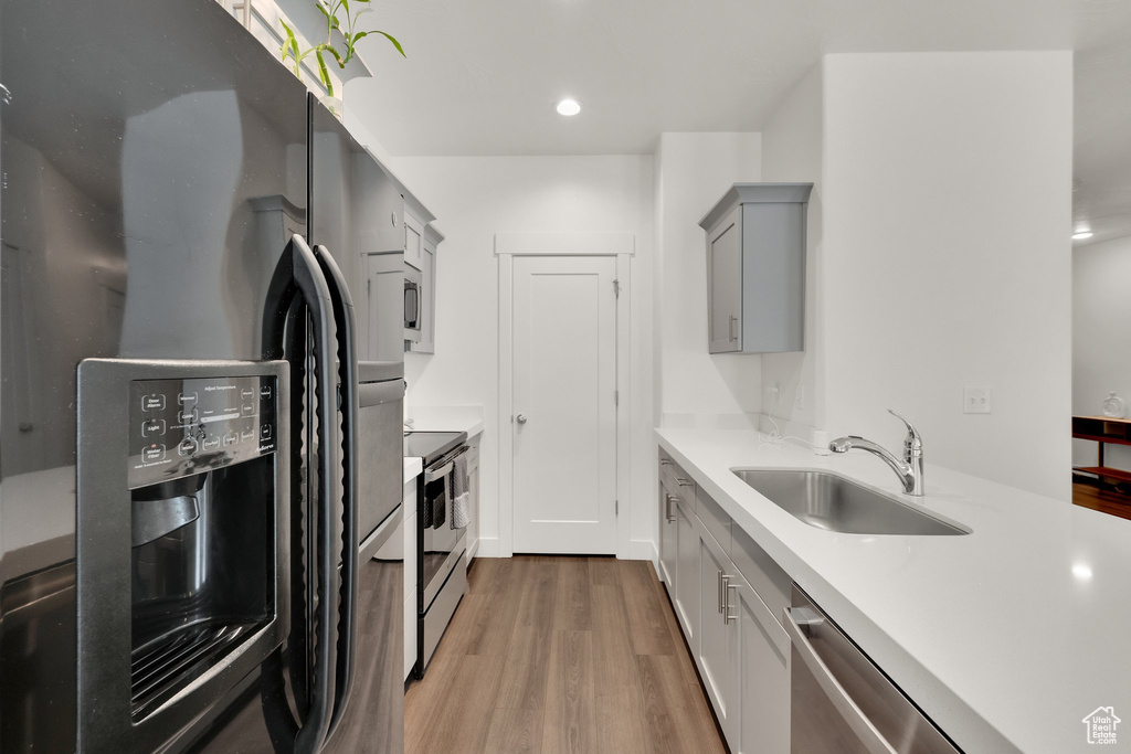 Kitchen featuring appliances with stainless steel finishes, a sink, gray cabinets, light wood-style flooring, and light countertops