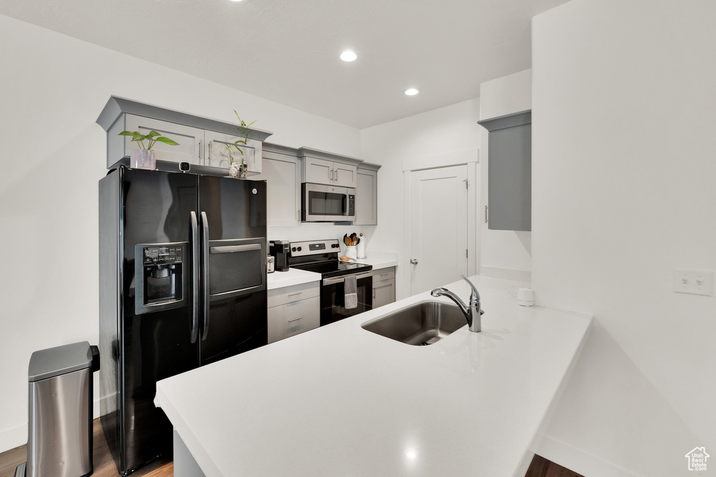 Kitchen featuring appliances with stainless steel finishes, a sink, gray cabinets, a peninsula, and light wood-style floors