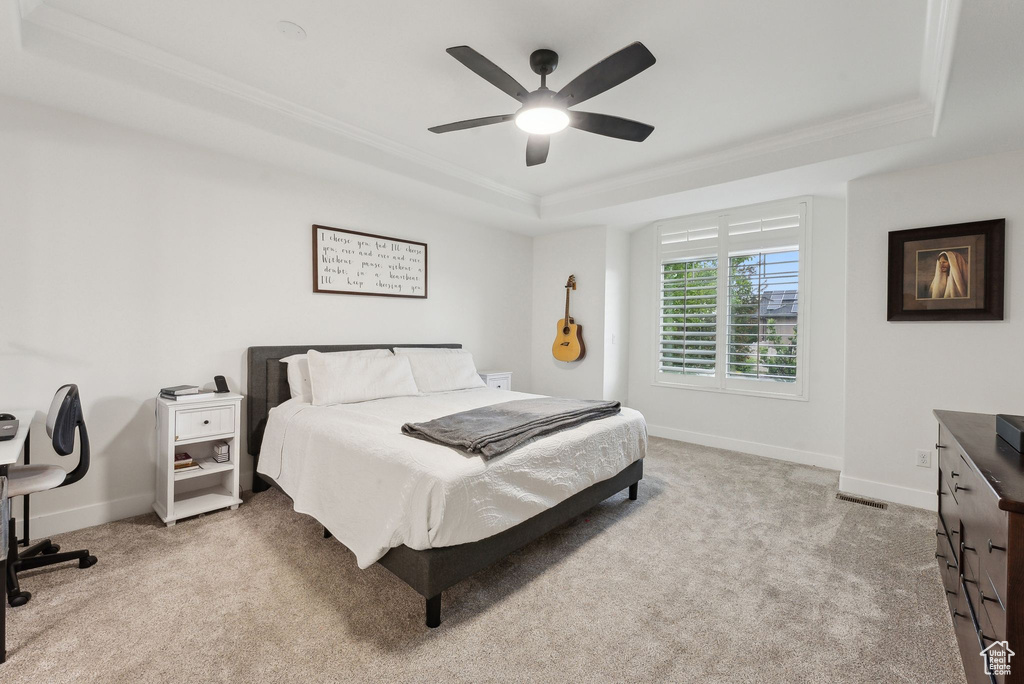 Carpeted bedroom featuring a tray ceiling, baseboards, crown molding, and a ceiling fan