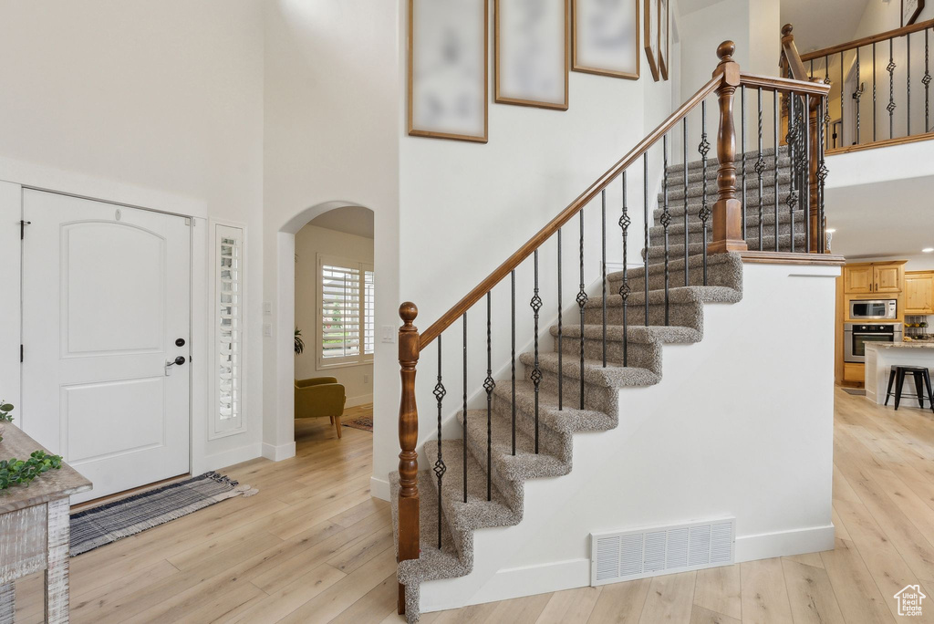 Entrance foyer featuring arched walkways, a towering ceiling, light wood-style flooring, and stairs